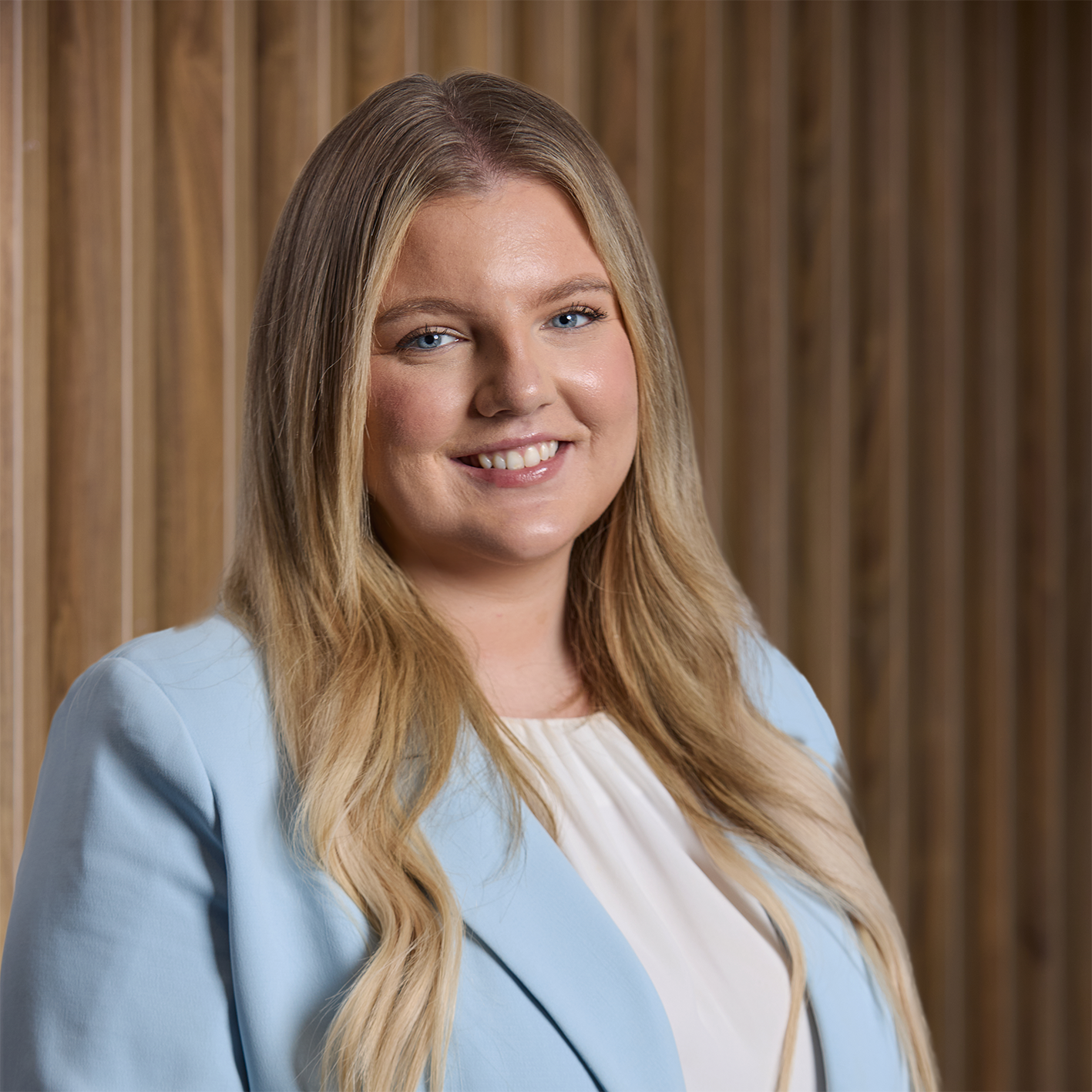 Headshot of Kate Hanlon in a blue jacket on wooden background