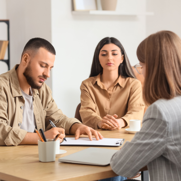 Image Shows: young couple signing document with a lawyer present