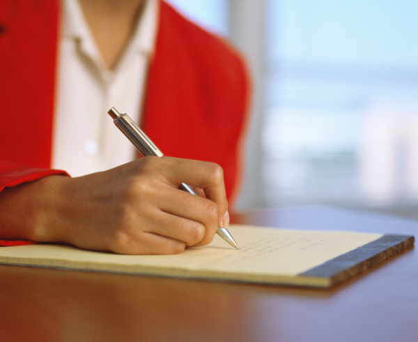 Image Shows: lawyer in red jacket taking notes at a meeting