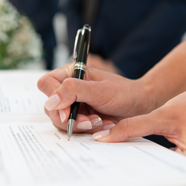 Image Shows: Hand holding a black pen about to sign a document