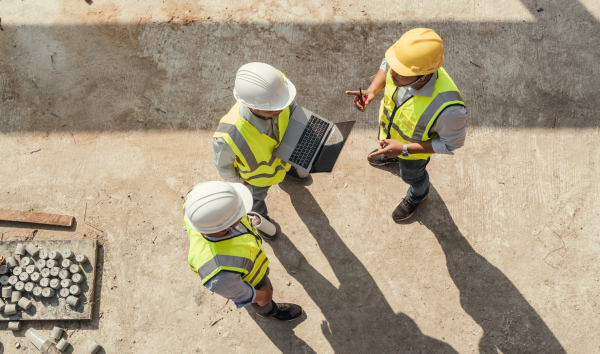 Three construction workers talking while holding a laptop