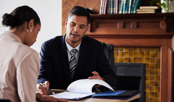 A lawyer sitting with a woman and pointing out something on the document with his pen