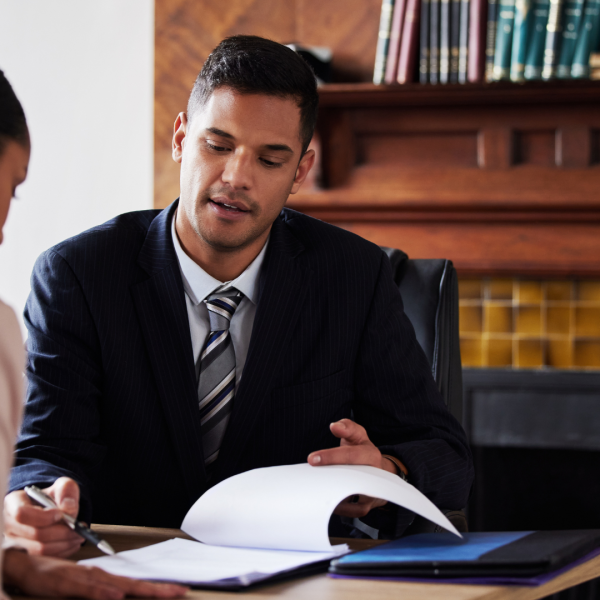 A lawyer sitting with a woman and pointing out something on the document with his pen