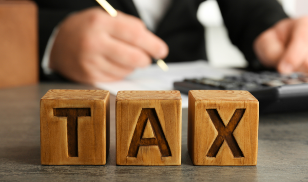 image shows employee in office writing on a document with the word 'TAX' in wooden blocks