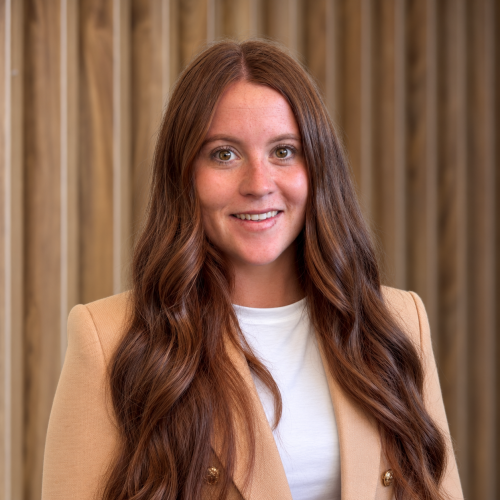 Photgraph of woman in camel jacket with long dark hair, wooden background